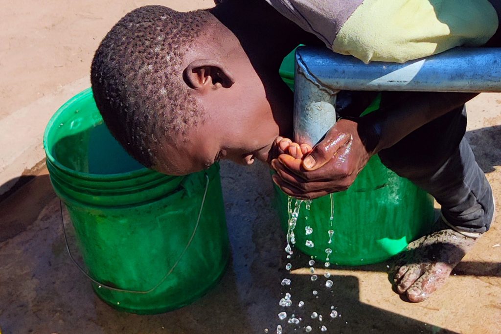 Boy drinking fresh water from a well.